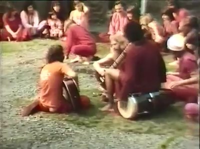 File:Osho at Chidvilas (1981) ; still 03min 19sec Swami Anand Nivedano sitting on drum (1).jpg
