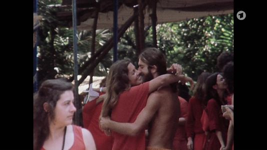 still 0h 20m 29s. Shows scene in the Ashram with people hugging