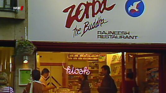 still 21m 43s. Shows kiosk of former „Zorba the Buddha“ restaurant in Cologne